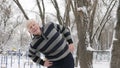 An elderly European man does a morning outdoor warm-up in the winter, exercise for the lower back, leanings forward