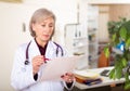 Elderly female doctor with papers studying clinical diagnosis of patient Royalty Free Stock Photo