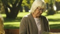 Elderly friends sitting apart after conflict, prying information in newspaper