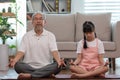 Elderly grandfather and children doing yoga for meditation together in living room at home so happy and comfortable