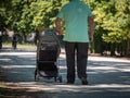 Elderly Grandfather Man Walking at Public Park dragging Stroller with one Hand