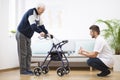 Elderly grandfather with walker trying to walk again and helpful male nurse supporting him