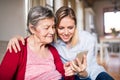 Elderly grandmother and adult granddaughter with smartphone at home.