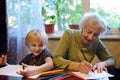 Elderly grandmother helping little grandchild doing homework. Grandma and grandson drawing together