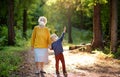 Elderly grandmother and little grandchild wearing facemask walking together in sunny summer park. Grandma and grandson. Lifting