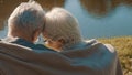 Elderly gray haired couple siting on the bench near the river covering with blanket on autumn day. Romance and old age Royalty Free Stock Photo