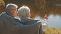 Elderly gray haired couple siting on the bench near the river covering with blanket on autumn day. Romance and old age Royalty Free Stock Photo