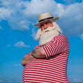 Elderly gray-haired man with a beard in a striped bathing suit and hat posing on the beach. Senior citizen on vacation Royalty Free Stock Photo