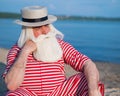 Elderly gray-haired man with a beard in a striped bathing suit and hat posing on the beach. Senior citizen on vacation Royalty Free Stock Photo