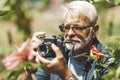 An elderly gray-haired man photographs a flower in the park, portrait Royalty Free Stock Photo