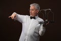 Elderly gray-haired man 50s, in white shirt, glasses and bow tie weighing something on scales with kettlebells