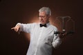 Elderly gray-haired man 50s, in white shirt, glasses and bow tie weighing something on scales with kettlebells