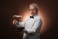 Elderly gray-haired man 50s, in white shirt, glasses and bow tie weighing something on scales with kettlebells