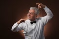 Elderly gray-haired man 50s, in white shirt, glasses and bow tie weighing something on scales with kettlebells