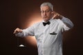 Elderly gray-haired man 50s, in white shirt, glasses and bow tie weighing something on scales with kettlebells