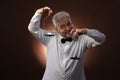 Elderly gray-haired man 50s, in white shirt, glasses and bow tie weighing something on scales with kettlebells