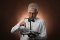 Elderly gray-haired man 50s, in white shirt, glasses and bow tie weighing something on scales with kettlebells