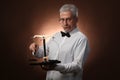 Elderly gray-haired man 50s, in white shirt, glasses and bow tie weighing something on scales with kettlebells