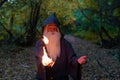 An elderly gray-haired witcher casts a fire spell in the forest. Man in wizard costume