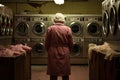 Elderly gray-haired woman in pink raincoat washes her clothes in public laundry. Generative AI Royalty Free Stock Photo