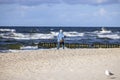 Elderly gray-haired woman walking on sand with trekking poles on shore of the Baltic Sea, Miedzyzdroje, Poland