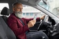 Elderly man driving new car, using mobile phone Royalty Free Stock Photo