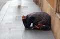 Elderly gypsy woman asking for alms kneeling on the ground with