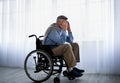 Elderly handicapped man in wheelchair covering face with hands, crying near windows, suffering from depression indoors