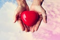 Elderly hands with wound holding red heart heart on colorful sky and white clouds, vintage tone Royalty Free Stock Photo