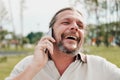 An elderly handsome man with long hair in the tail emotionally speaks on a cell phone in a park on a bench.