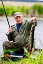 An elderly fisherman in camouflage shows the catch. Opening of the fishing season.