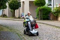 An elderly happy lady rides a four-wheeled electric scooter for the disabled on the street of the old German city. Image of active