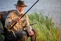 Elderly happy man fishing outside in evening on lake in summer sitting on chair Royalty Free Stock Photo