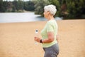 Elderly happy retired woman jogging. An old woman runs along the beach and holds a bottle of water. Royalty Free Stock Photo