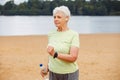 Elderly happy retired woman jogging. An old woman runs along the beach and holds a bottle of water. Royalty Free Stock Photo