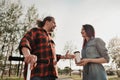 An elderly hipster man with long hair and a beard in a red plaid shirt is talking to a young woman. Summer warm evening Royalty Free Stock Photo