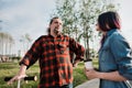 An elderly hipster man with long hair and a beard in a red plaid shirt is talking to a young woman. Summer warm evening Royalty Free Stock Photo