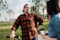 An elderly hipster man with long hair and a beard in a red plaid shirt is talking to a young woman. Summer warm evening Royalty Free Stock Photo