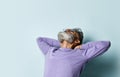 Gray-haired man in purple sweater, sunglasses. Put his hands behind head and looking up, posing on blue background. Close up Royalty Free Stock Photo