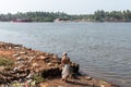 An elderly Indian man dressed in traditional Brahmin attire standing on the banks of the