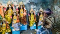 An elderly Indian man smoking a bidi at his sculpture workshop with idols of the Hindu