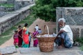 An elderly Indian street vendor sitting on the stone walls of the Vellore Fort