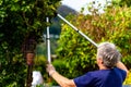 Elderly lady Cutting tree doing home garden work with long tree cutters. Royalty Free Stock Photo