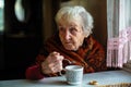 An elderly lady drinking tea sitting at a table in the house. Help. Royalty Free Stock Photo