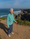 Elderly lady in her eighties with walking stick by beautiful coast scene with wind blowing through her hair Royalty Free Stock Photo