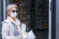 Elderly lady with mask and protective gloves leaves the chemist`s shop with medicines and instructions. Fear of coronavirus