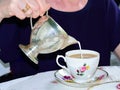 Elderly lady pouring milk into vintage bone china cup. No face visible. Concept of Mother`s Day. Concept of aging and elderly car