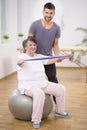 Elderly siting on the exercise ball during physiotherapy with her young instructor