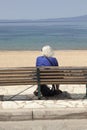 Elderly lady sits alone on bench and looks at the sea in greece