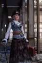 Elderly lady in a steampunk costume at an abandoned factory with arms in hand